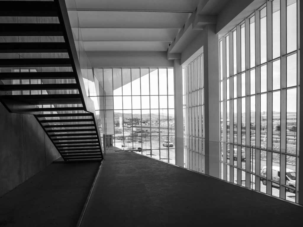 Black and white photo of Modula's New Fiorano Facility interior with large windows, a staircase, and an outdoor view through the glass.