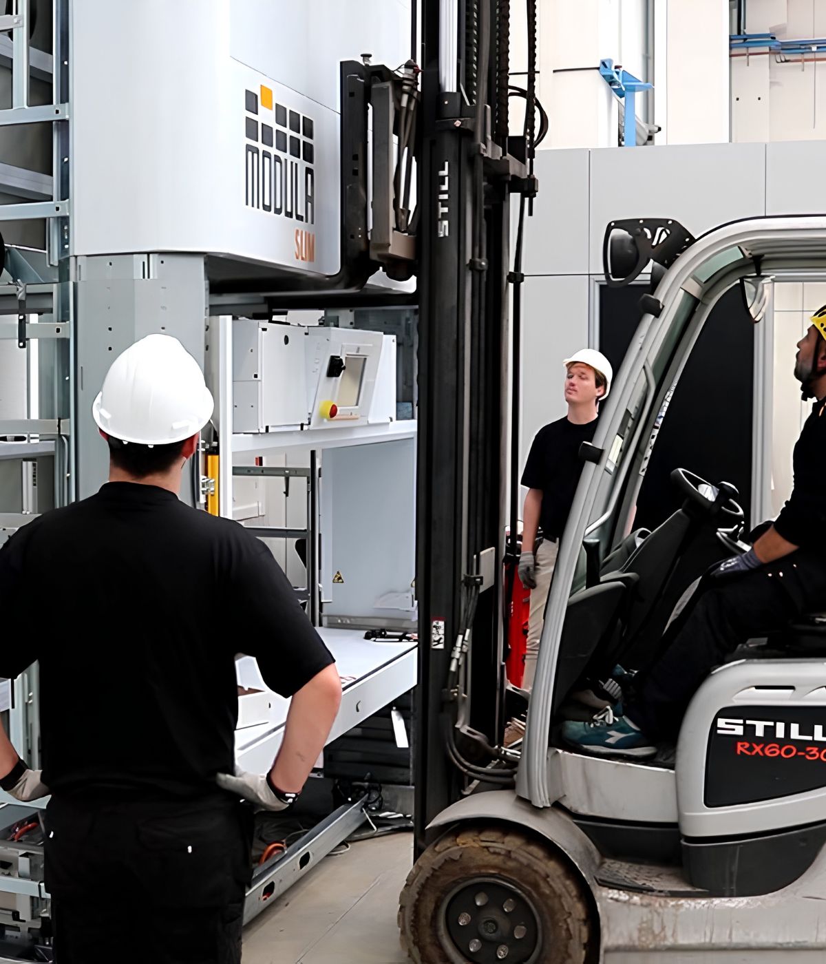 Three workers in a warehouse operate a forklift near a large industrial storage system during a New Consulting site visit.