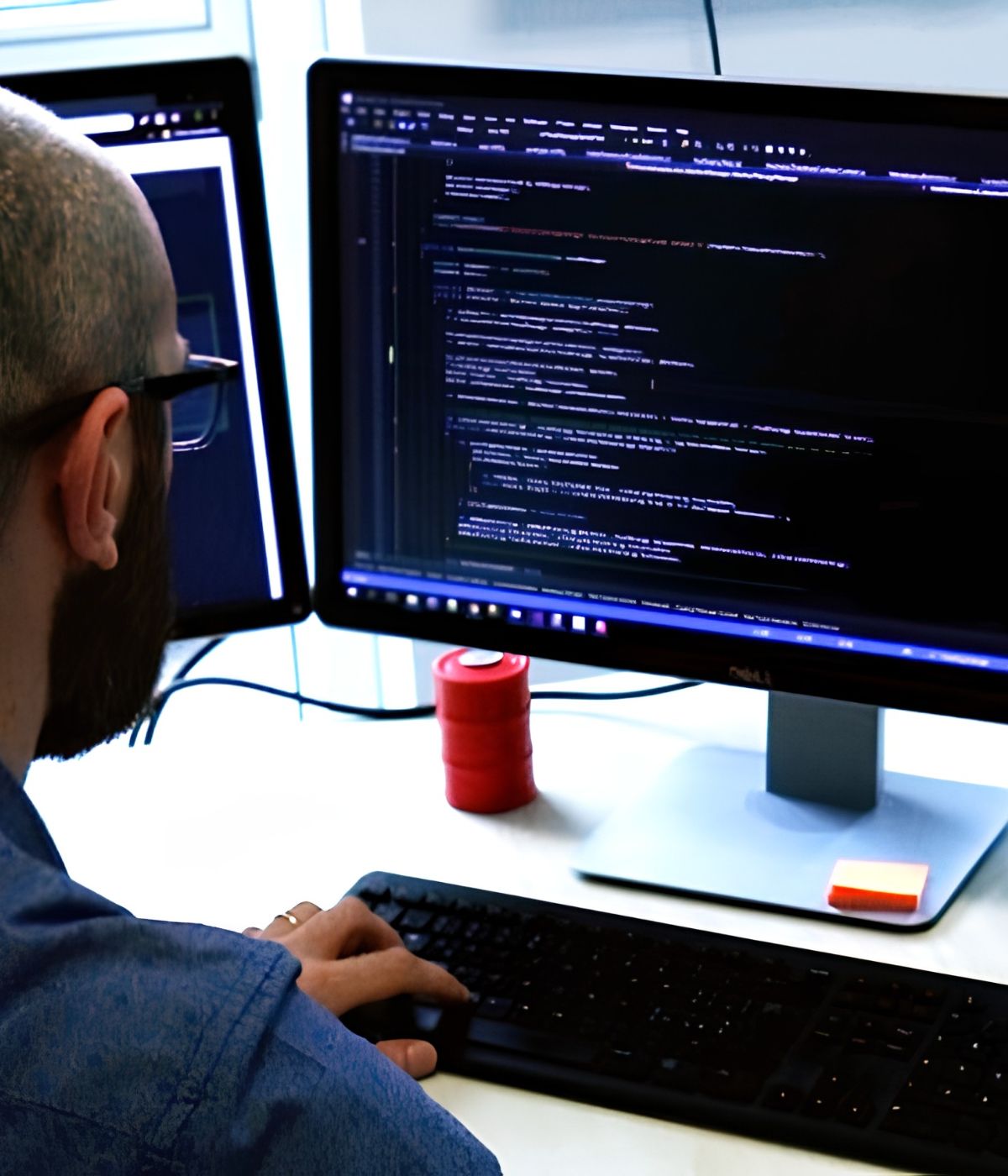 A person sits at a desk working on programming code, providing consulting services with a secondary screen nearby.